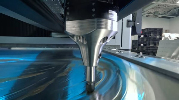 A large silver cone attached to a black hemisphere floats over a piece of sheet metal held in a metal frame. The metal has what appears to be machine grease on it to aid in the forming process.